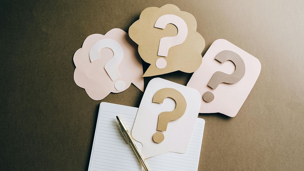 Paper question-mark speech bubbles beside a notebook and pen